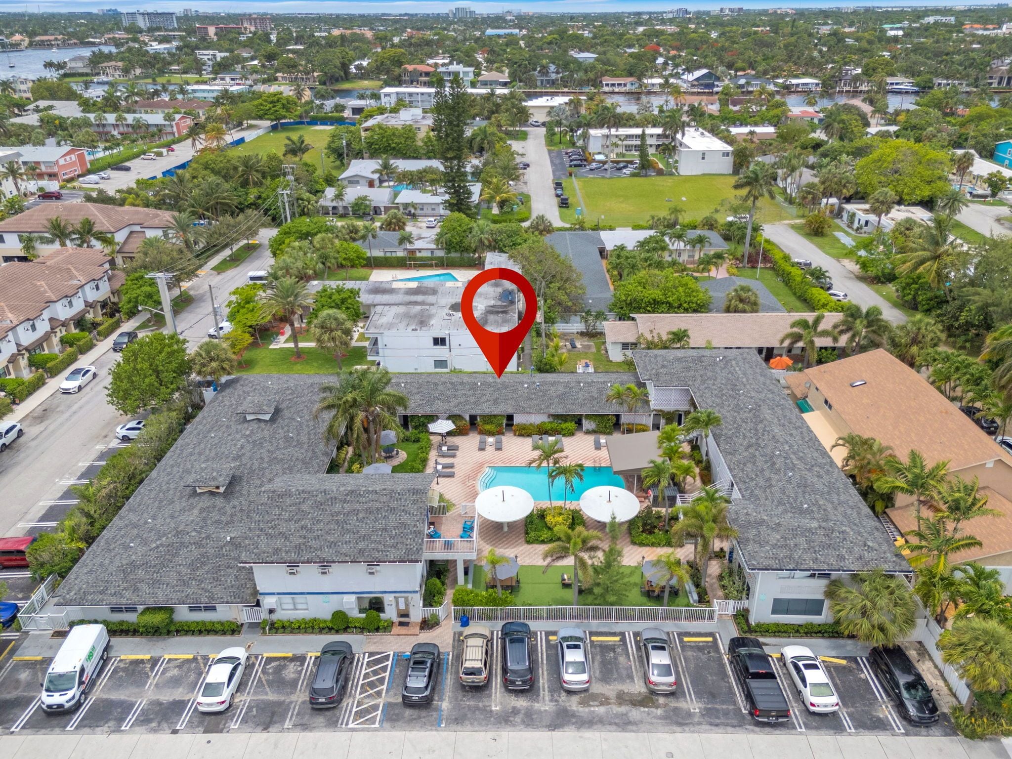 A hotel with a swimming pool, multiple parking spaces, and a view of the surrounding neighborhood.
