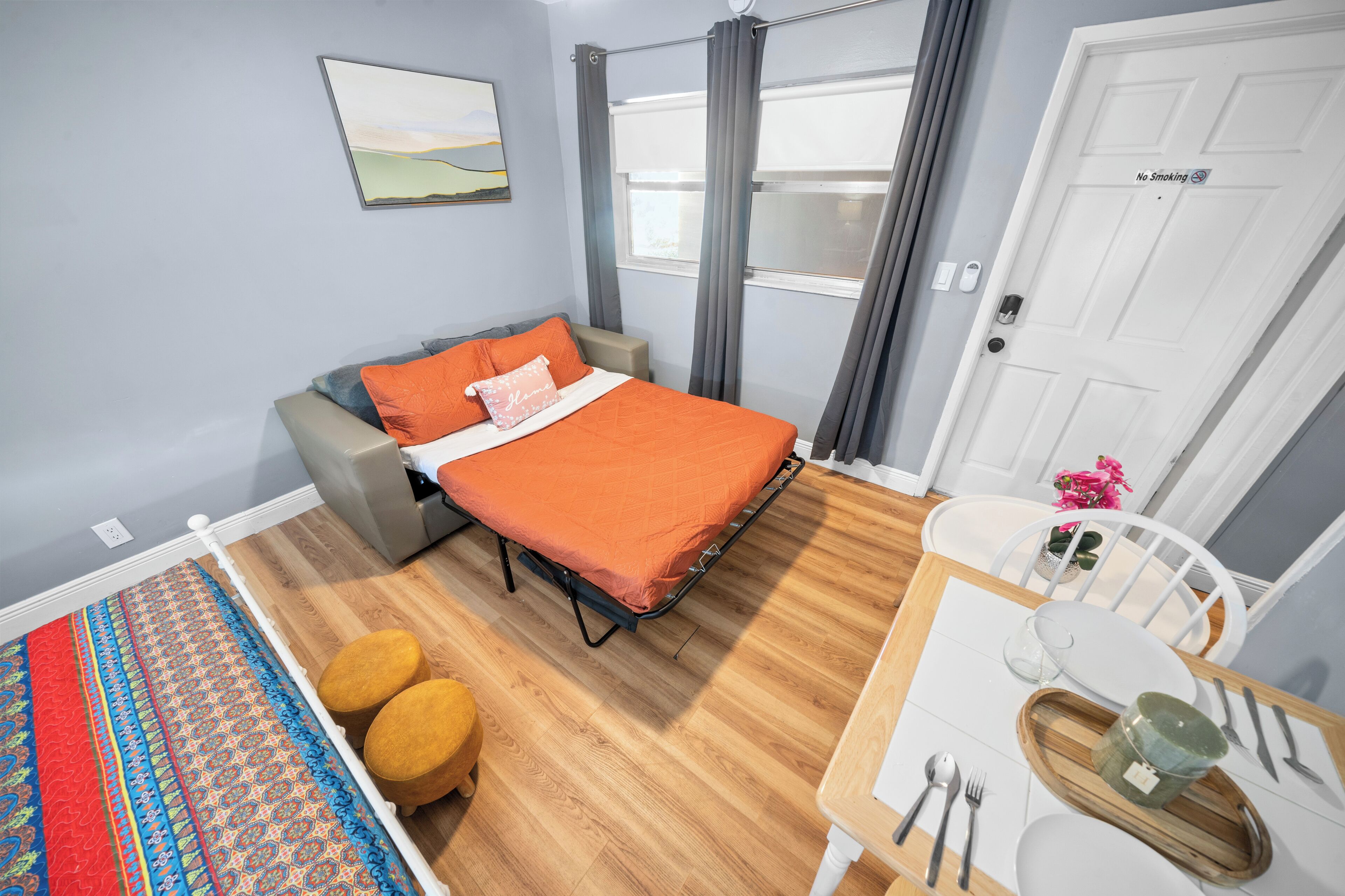 Une pièce de taille modeste comprenant un lit, un petit canapé, une table à manger avec des chaises et une fenêtre avec des rideaux.
