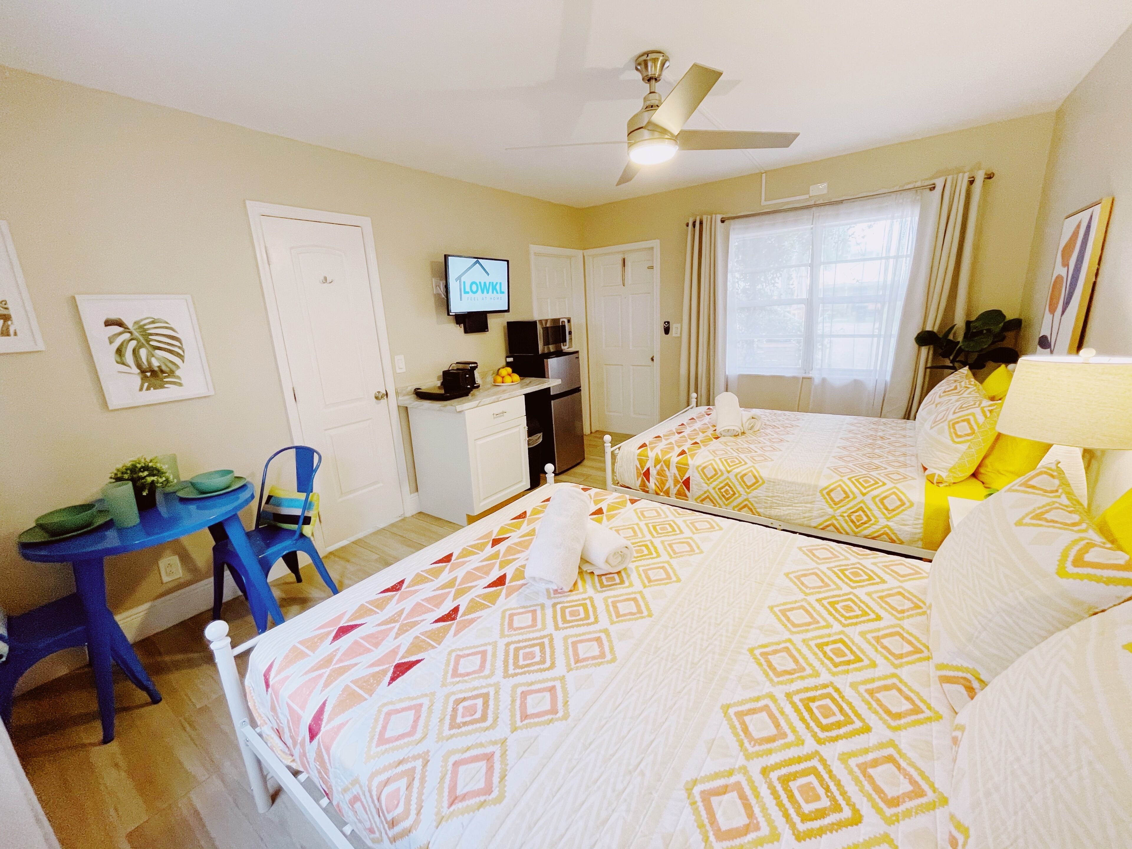 A hotel room with two beds, a desk, a chair, a TV, and a ceiling fan.