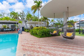 A poolside area with a swing chair, a covered seating area, and a building with a sign. - Sea Steps by Lowkl (Pompano Beach)