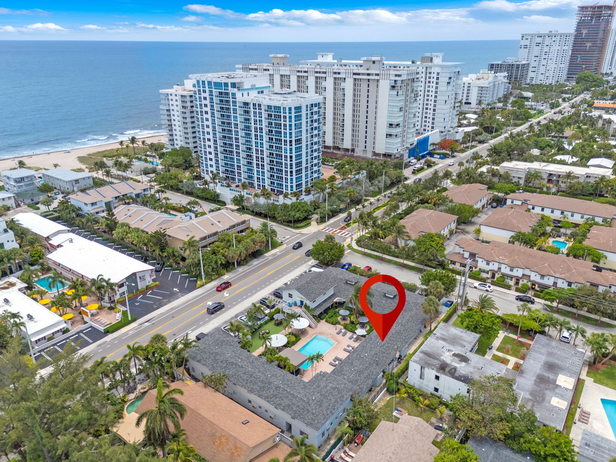An aerial view of a coastal urban area with high-rise buildings, a beach, and a marked location.