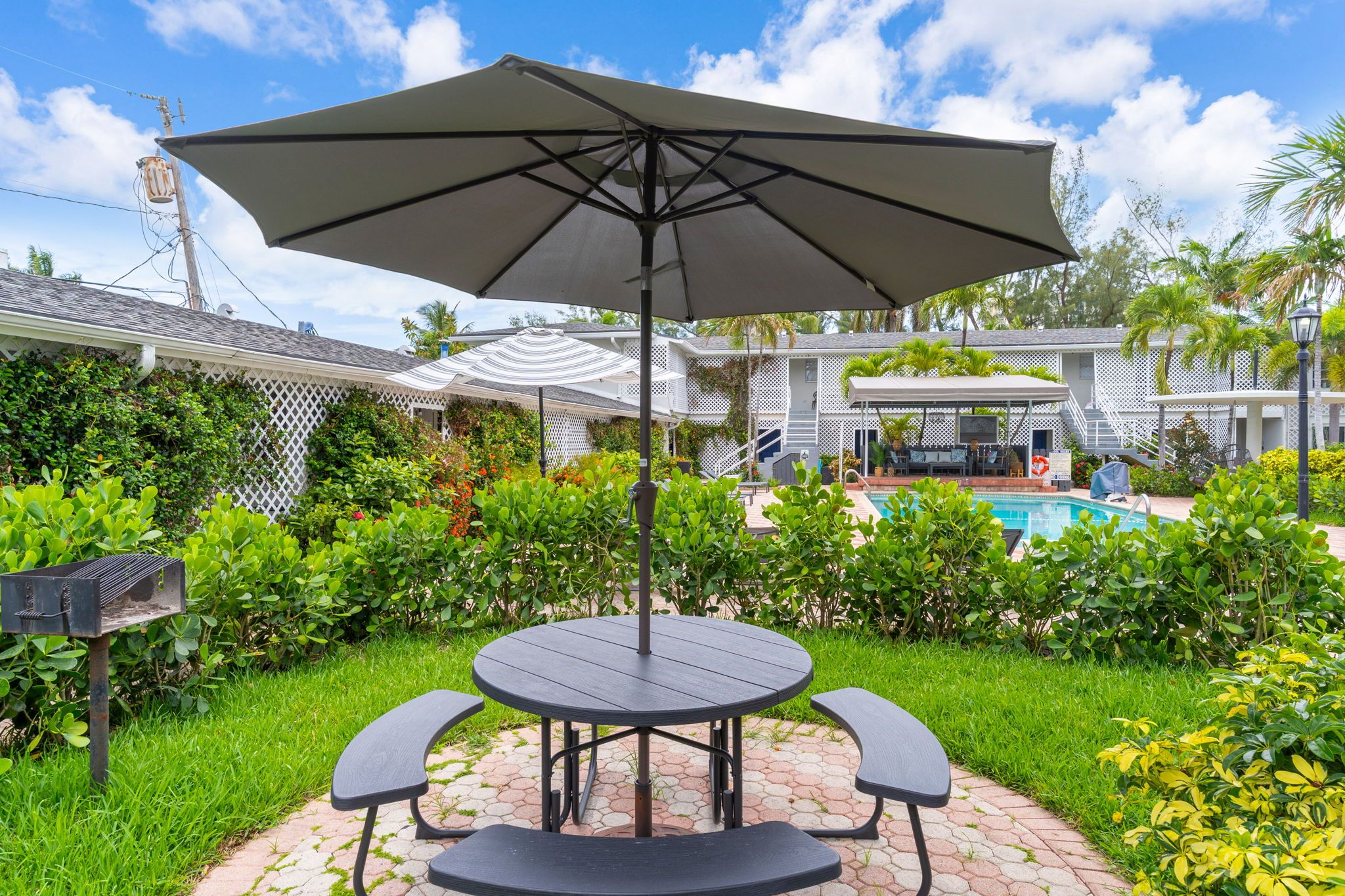 Een terras met een ronde tafel en twee stoelen, een parasol en een zwembad op de achtergrond.