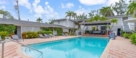 A swimming pool with a red and beige tiled deck, surrounded by lounge chairs and a covered seating area with a sign that reads 'Spa Studio.'