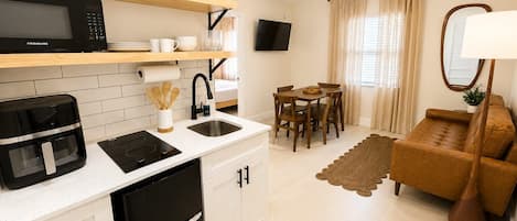 A compact kitchen with a microwave, coffee maker, and a refrigerator. There is a dining area with a table and chairs, and a sofa in the living room.
