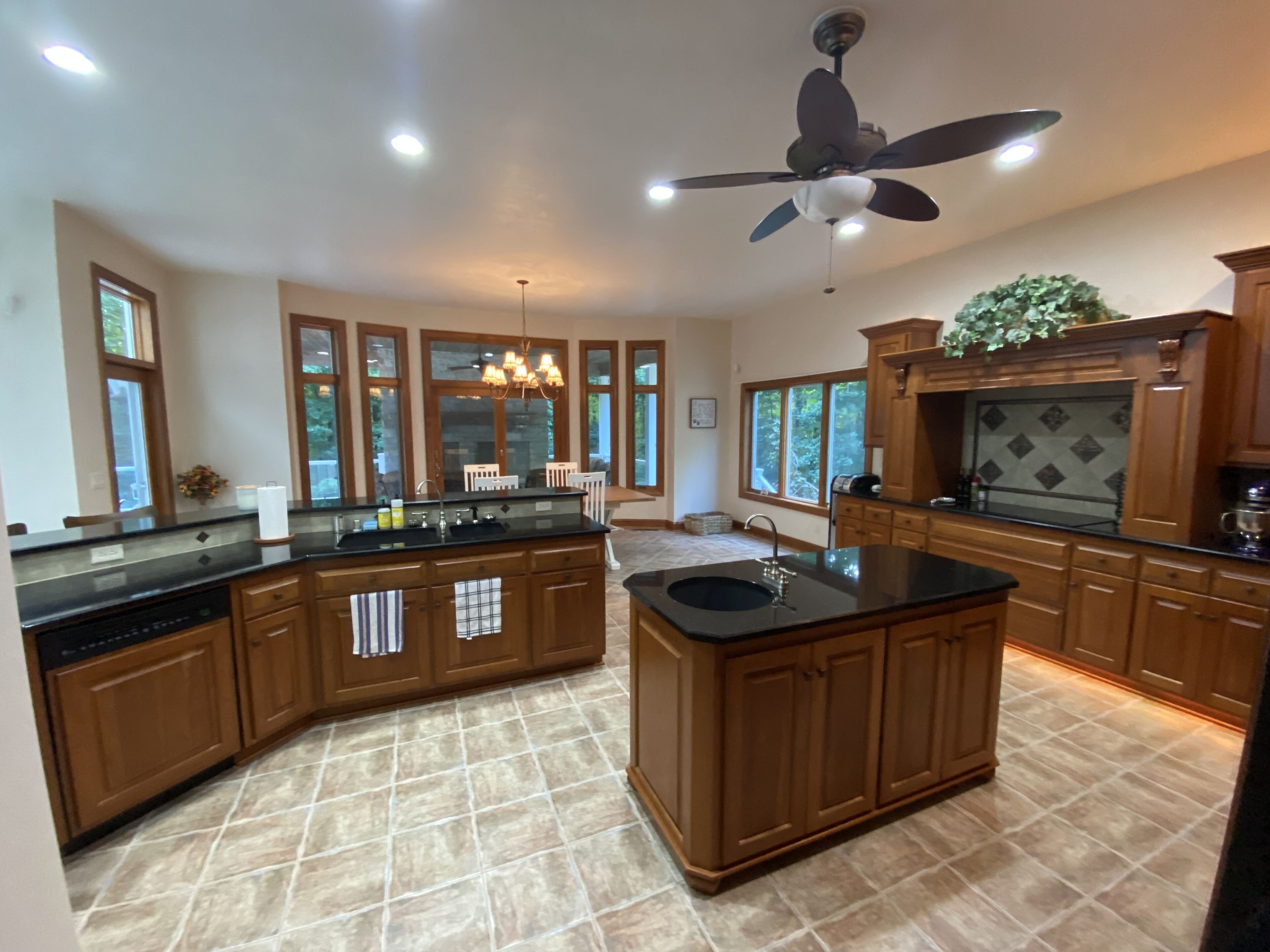 A spacious kitchen with a central island, wooden cabinets, a ceiling fan, and large windows.