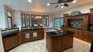 A spacious kitchen with a central island, wooden cabinets, a ceiling fan, and large windows. - Luxury Retreat in Ellison Bay (Ellison Bay)
