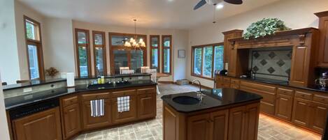 A spacious kitchen with a central island, wooden cabinets, a ceiling fan, and large windows.