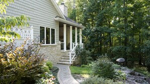 A house with a stone exterior, a covered porch with steps, and a garden with a pathway leading to the house. - Luxury Retreat in Ellison Bay (Ellison Bay)