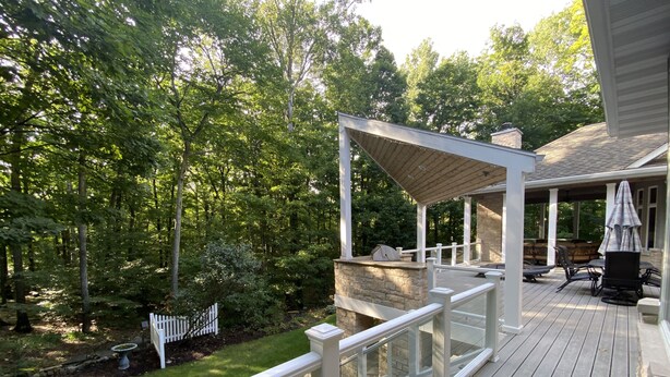 A wooden deck with a pergola, outdoor seating, and a stone fireplace. - Luxury Retreat in Ellison Bay (Ellison Bay)