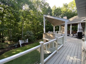 A wooden deck with a pergola, outdoor seating, and a stone fireplace. - Luxury Retreat in Ellison Bay (Ellison Bay)
