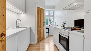 A modern kitchen with white cabinetry, a wooden door, a window, and a stove. - 1 bedroom cozy apartment in Aarhus C (Aarhus C)