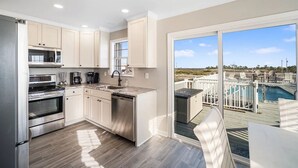 A modern kitchen with stainless steel appliances, a dishwasher, and a large window overlooking a pool and deck area. - Awesome views of the Gulf, Easy walk to the beach and Private  Pool! (Gulf Shores)