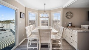 A dining area with a large table and white chairs, a chandelier, and a clock on the wall. - Awesome views of the Gulf, Easy walk to the beach and Private  Pool! (Gulf Shores)