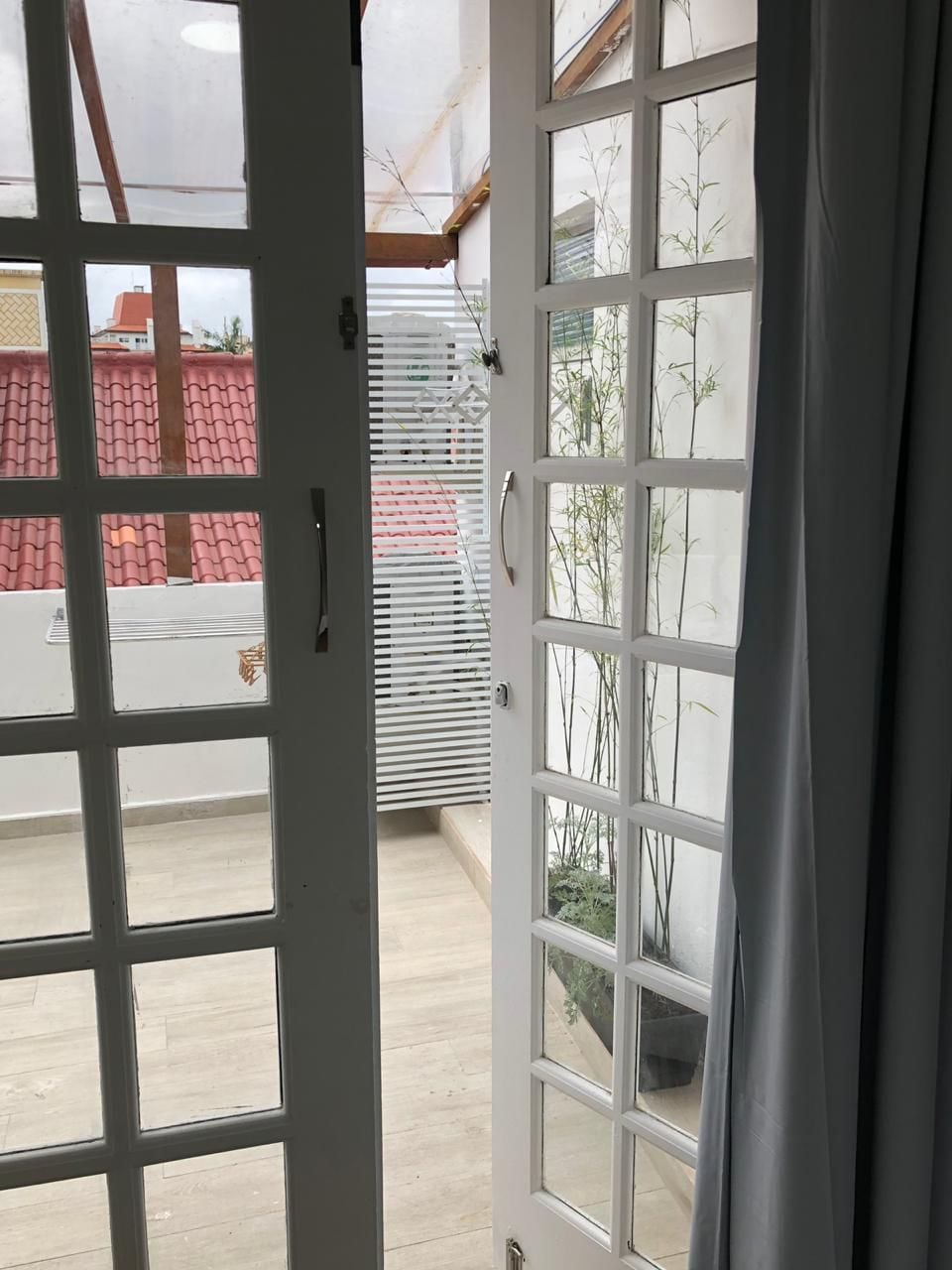 A view through a glass door leading to a balcony with a tiled roof, a metal railing, and a view of a building with a red roof.