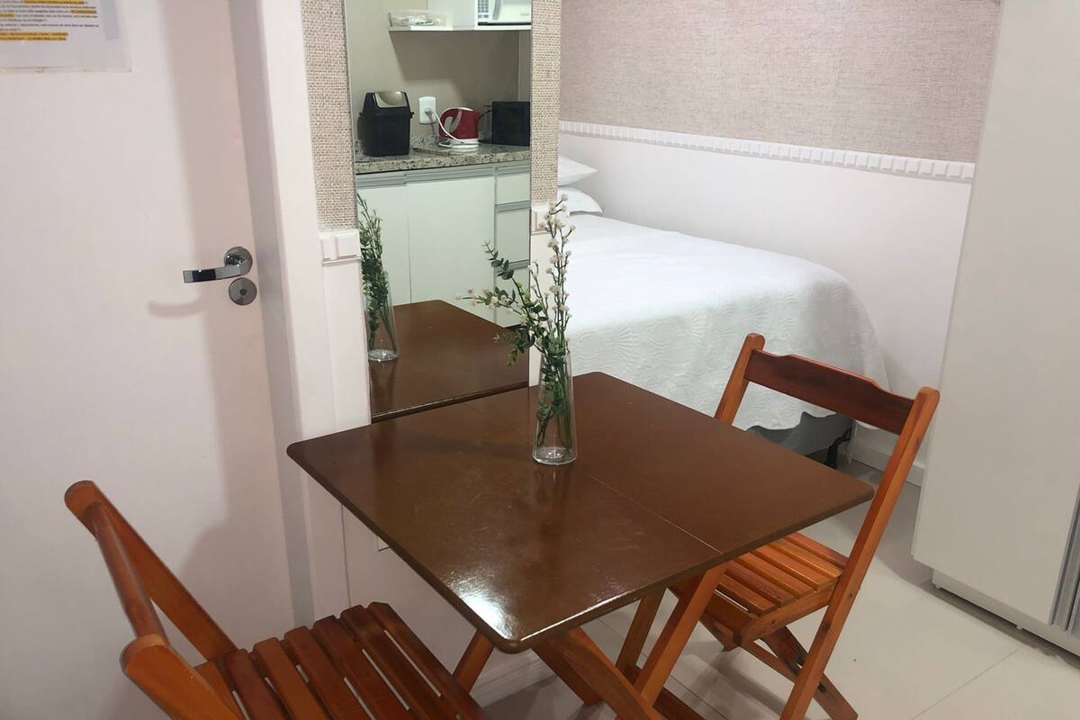 A small, neatly arranged room with a bed, a table, and two chairs.