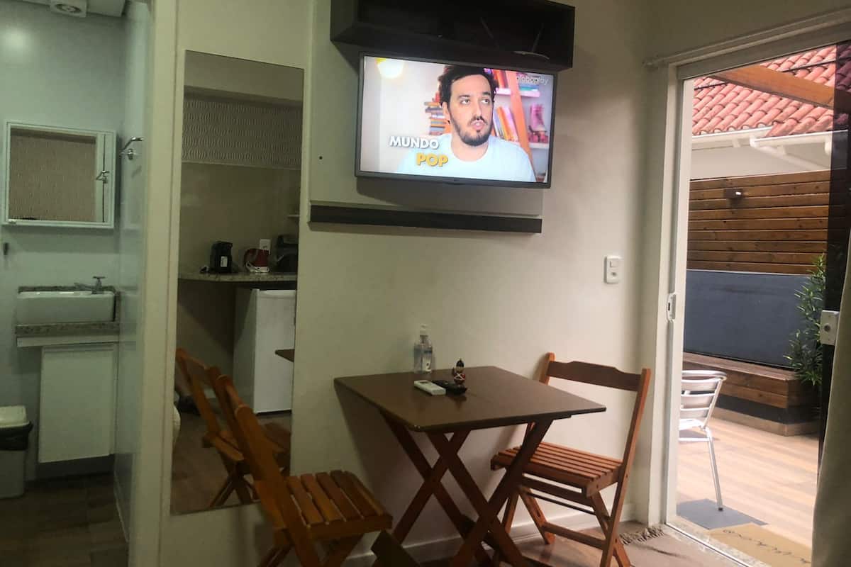 A small kitchen with a sink, a table with chairs, and a television mounted on the wall.