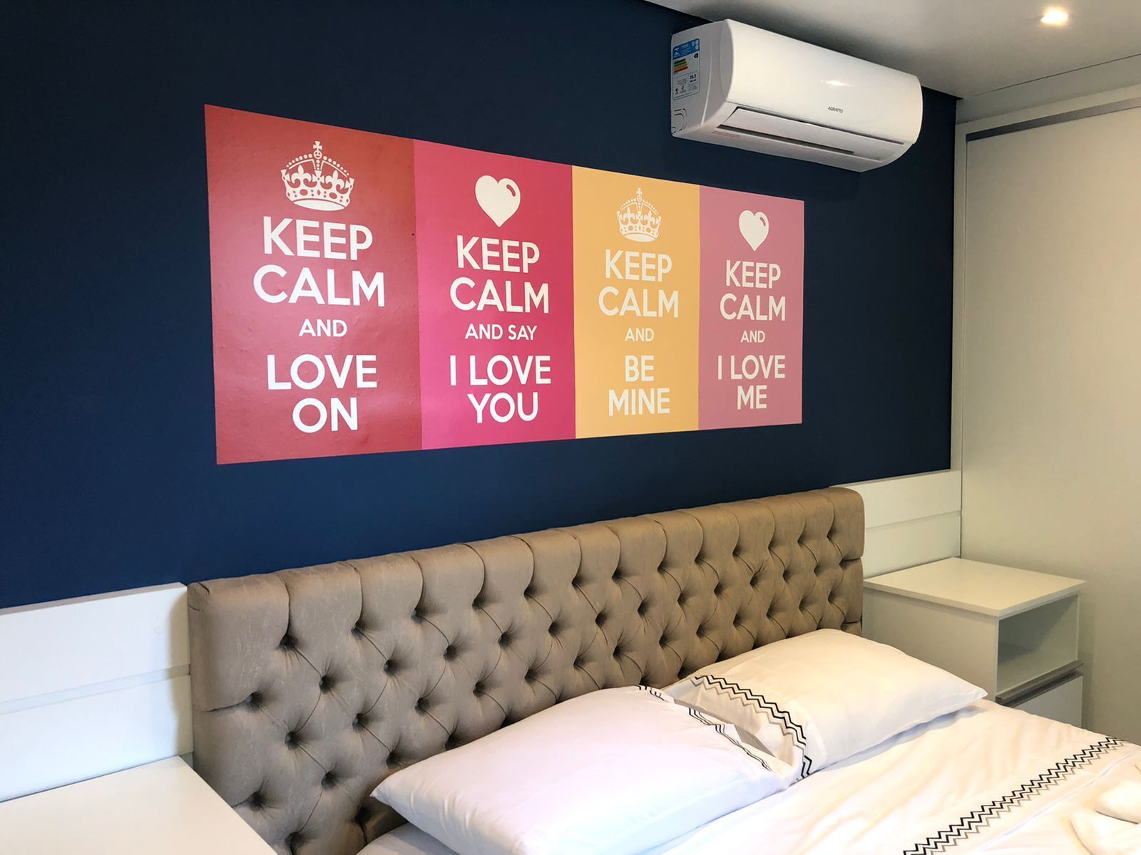 A hotel room with a bed, a tufted headboard, and a wall with four motivational posters.