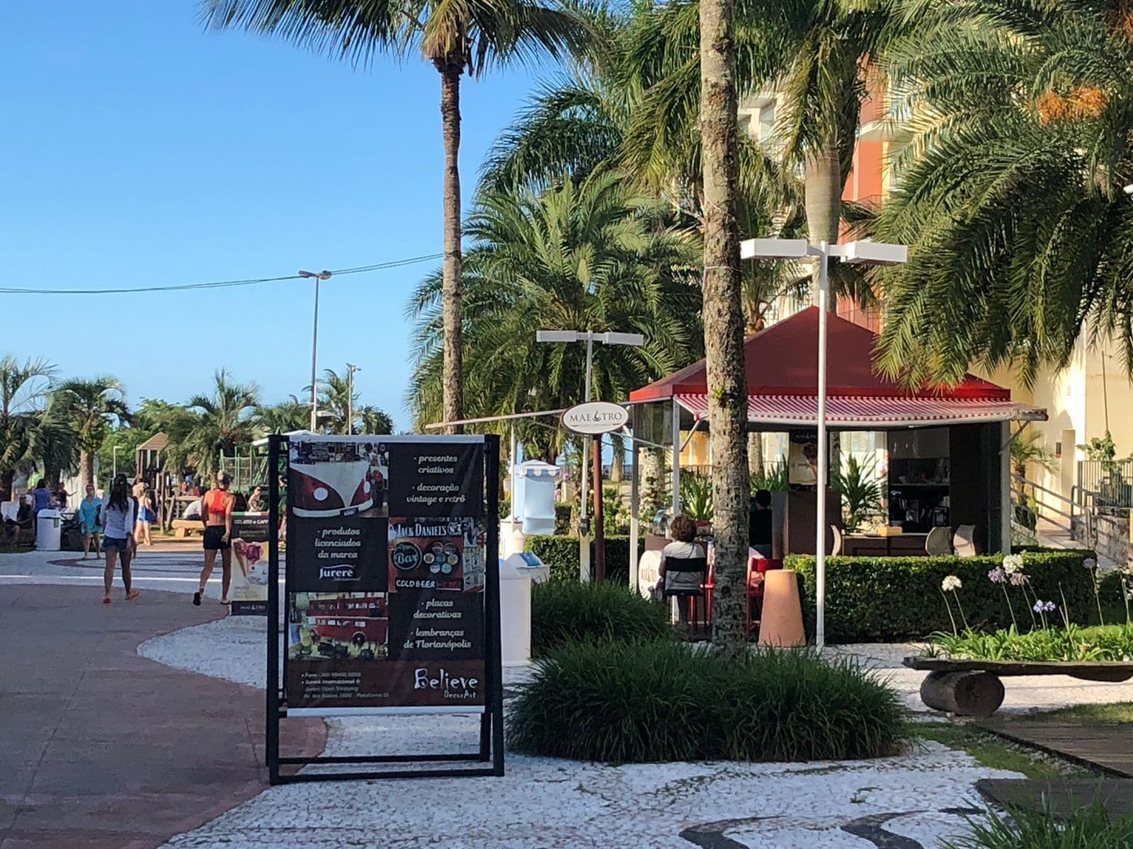 A signboard with various products and services, a palm tree-lined street, and a building with a red roof.