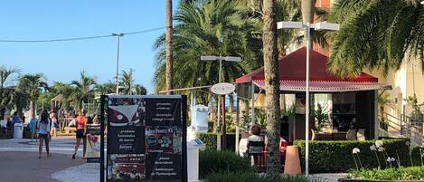 A signboard with various products and services, a palm tree-lined street, and a building with a red roof.