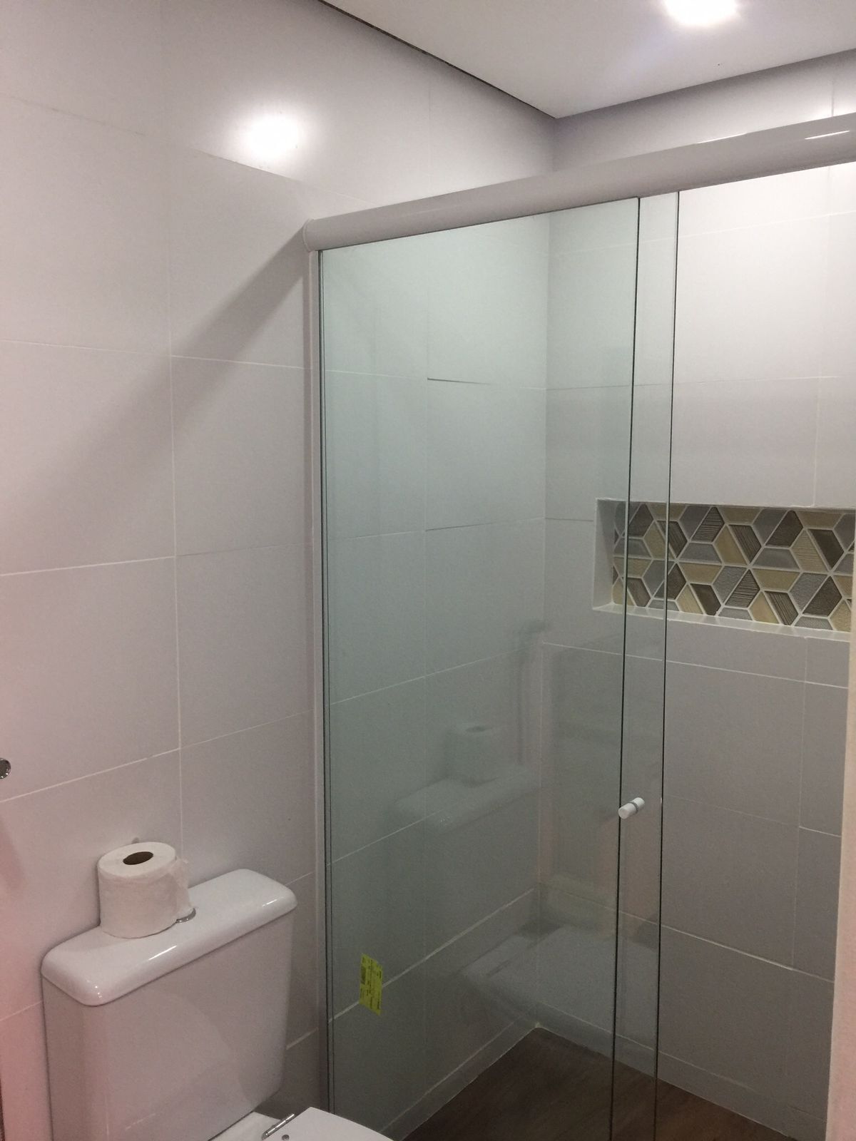 Ein modernes Badezimmer mit einer Duschkabine aus Glas, weißen Fliesen und einem WC mit Papierhandtuchspender.
