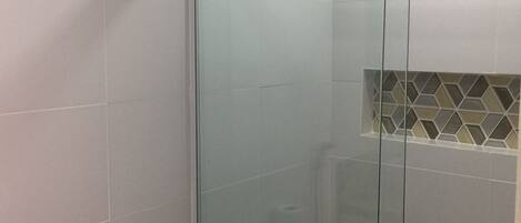 A modern bathroom with a glass shower enclosure, white tiles, and a toilet with a paper towel dispenser.