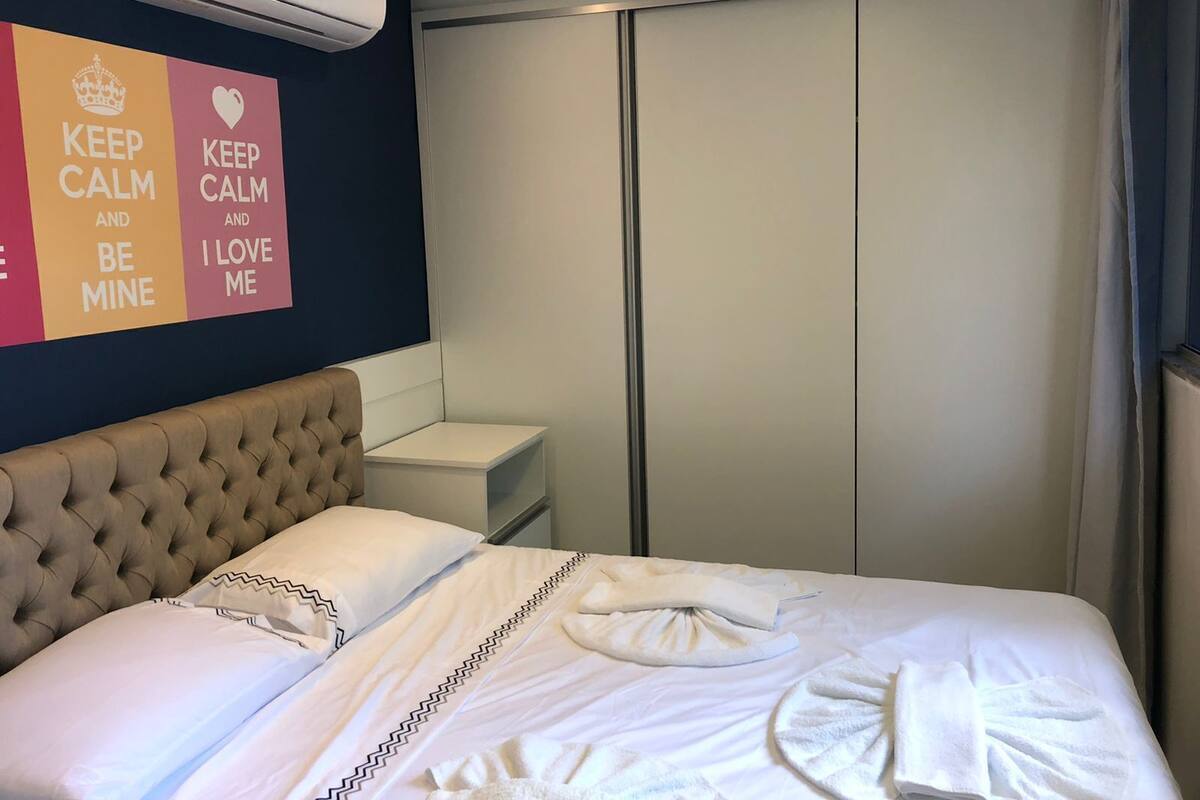 A hotel room with a bed, a bedside table, an air conditioning unit, and a wardrobe.