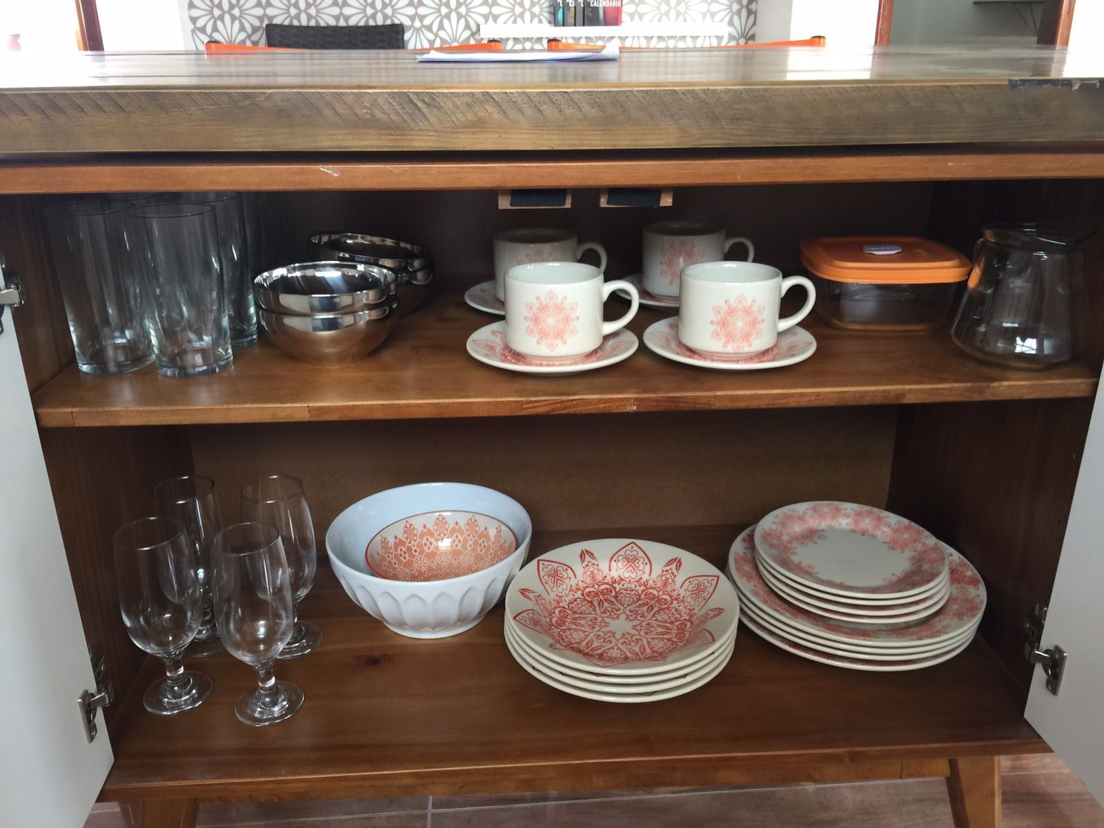 Una estantería de cocina con distintos vasos, incluyendo copas de vino, un tazón y platos apilados.