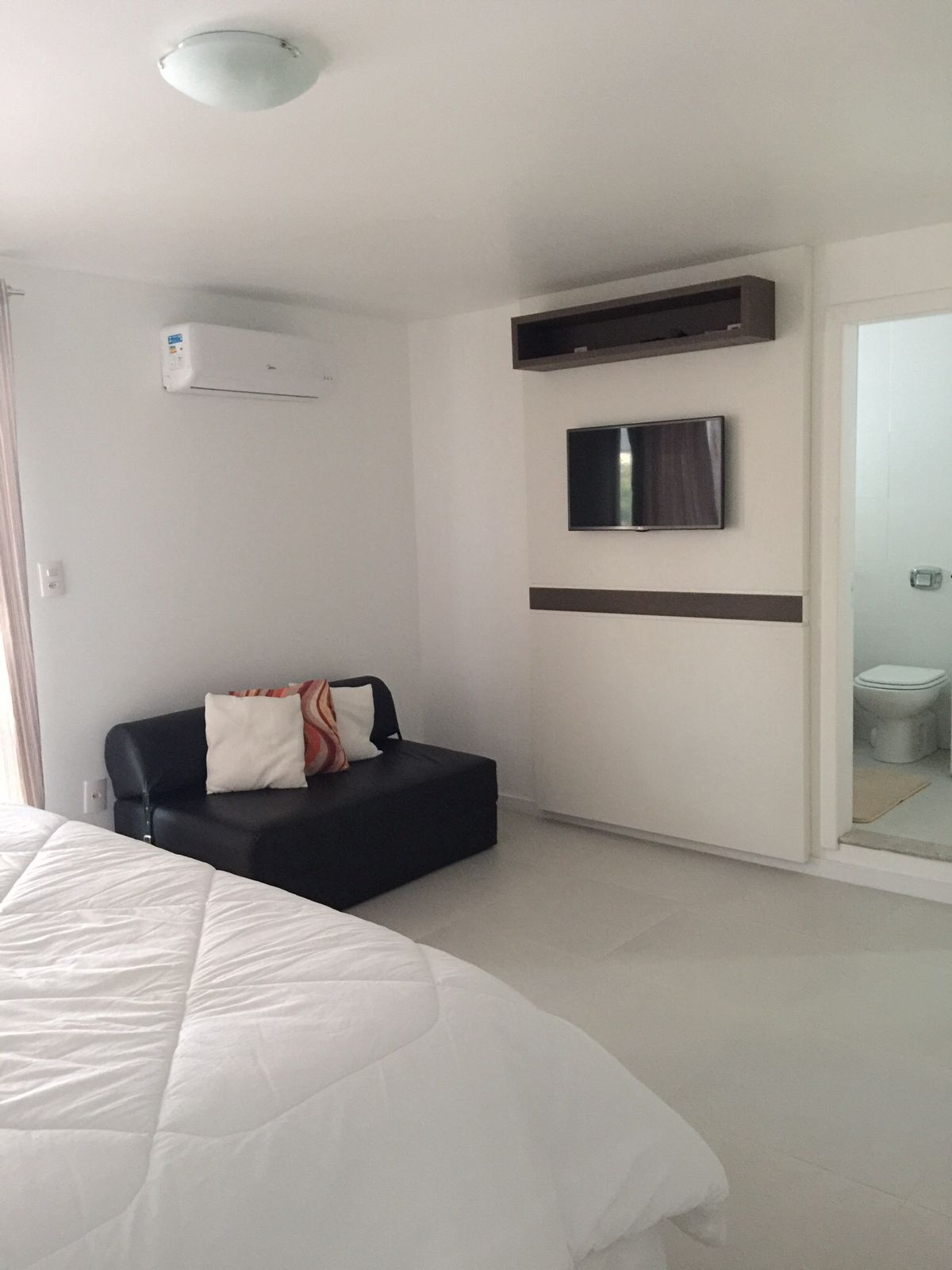 Una habitación de hotel con una cama, un sofá, un televisor montado en la pared y un equipo de aire acondicionado.
