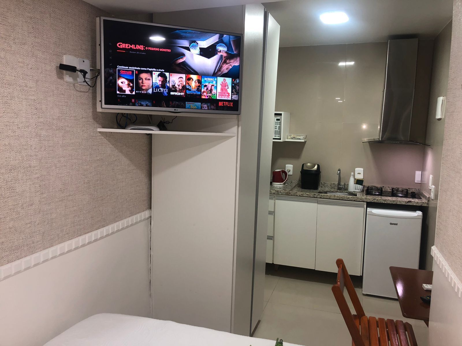 Une chambre d’hôtel équipée d’une télévision diffusant un film, d’une kitchenette avec un four à micro-ondes et d’un coin repas comprenant une chaise et une table.