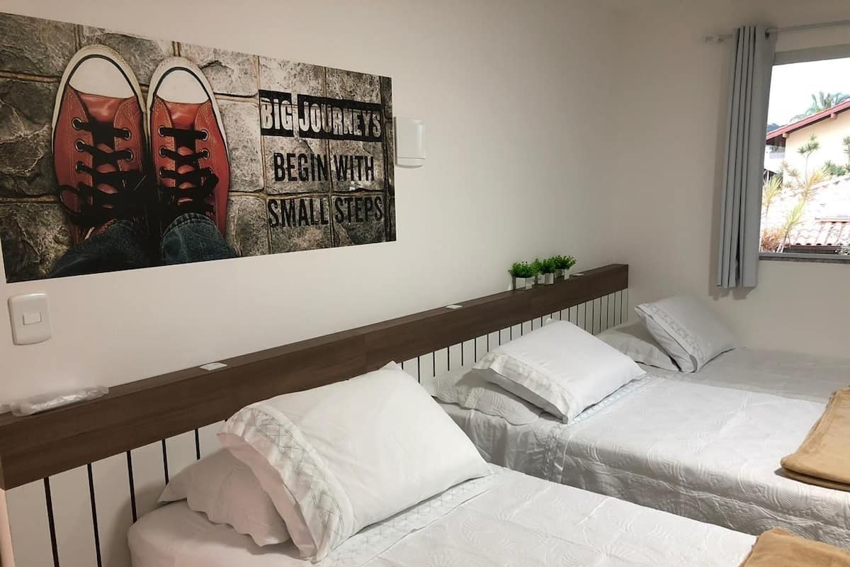 A hotel room with two beds, white bedding, a wooden headboard, a motivational poster, and a window with curtains.