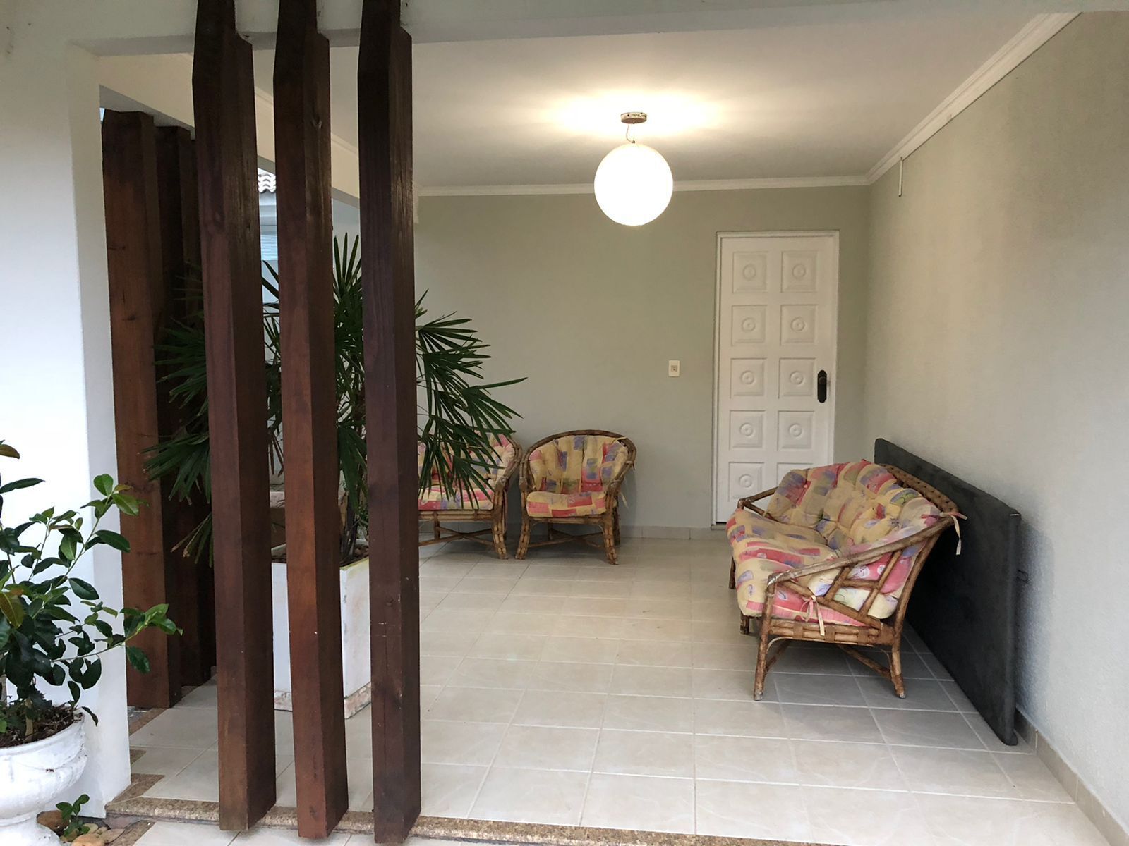A spacious living area with two wicker chairs, a sofa, and a potted plant.