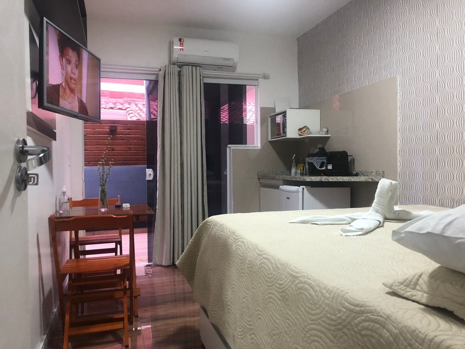 A hotel room with a bed, a desk, a chair, a TV, and a kitchenette.