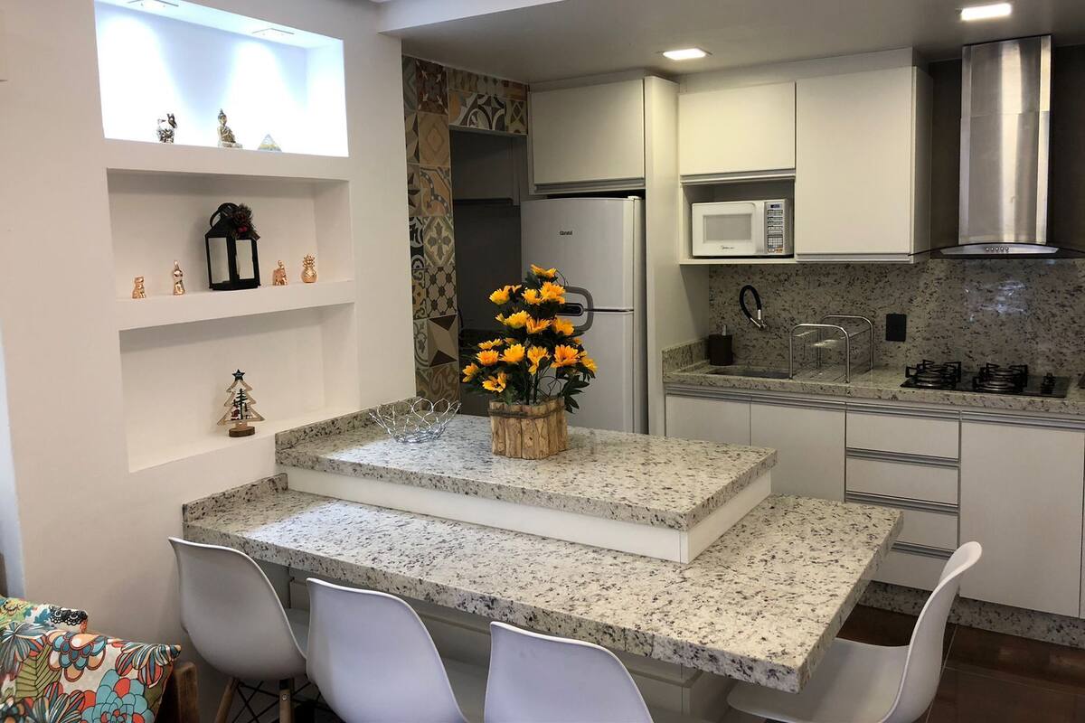 A modern kitchen with white cabinetry, a granite countertop, a built-in microwave, and a stainless steel range hood.