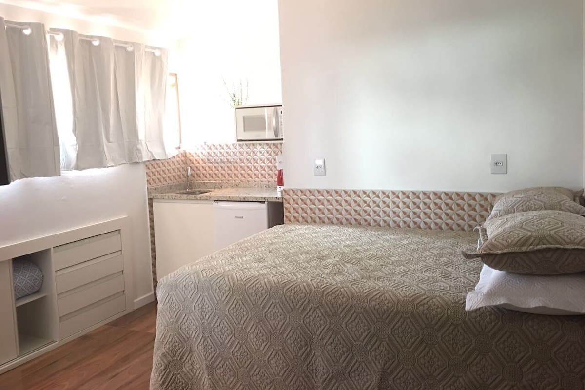 A bedroom with a bed, a bedside table, a wardrobe, and a kitchenette area with a microwave.
