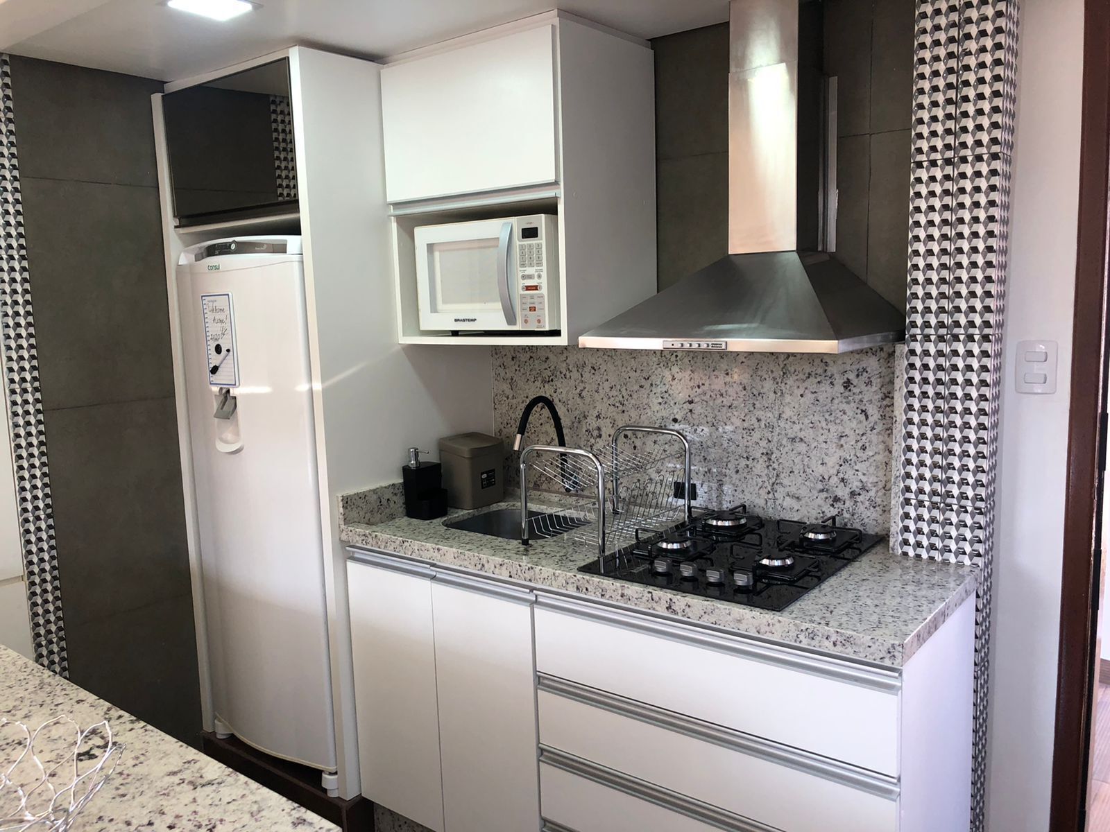 Una cocina moderna con refrigerador empotrado, microondas, estufa a gas y pileta de acero inoxidable.