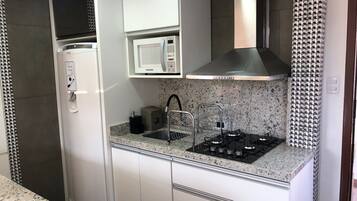 Una cocina moderna con refrigerador empotrado, microondas, estufa a gas y pileta de acero inoxidable.