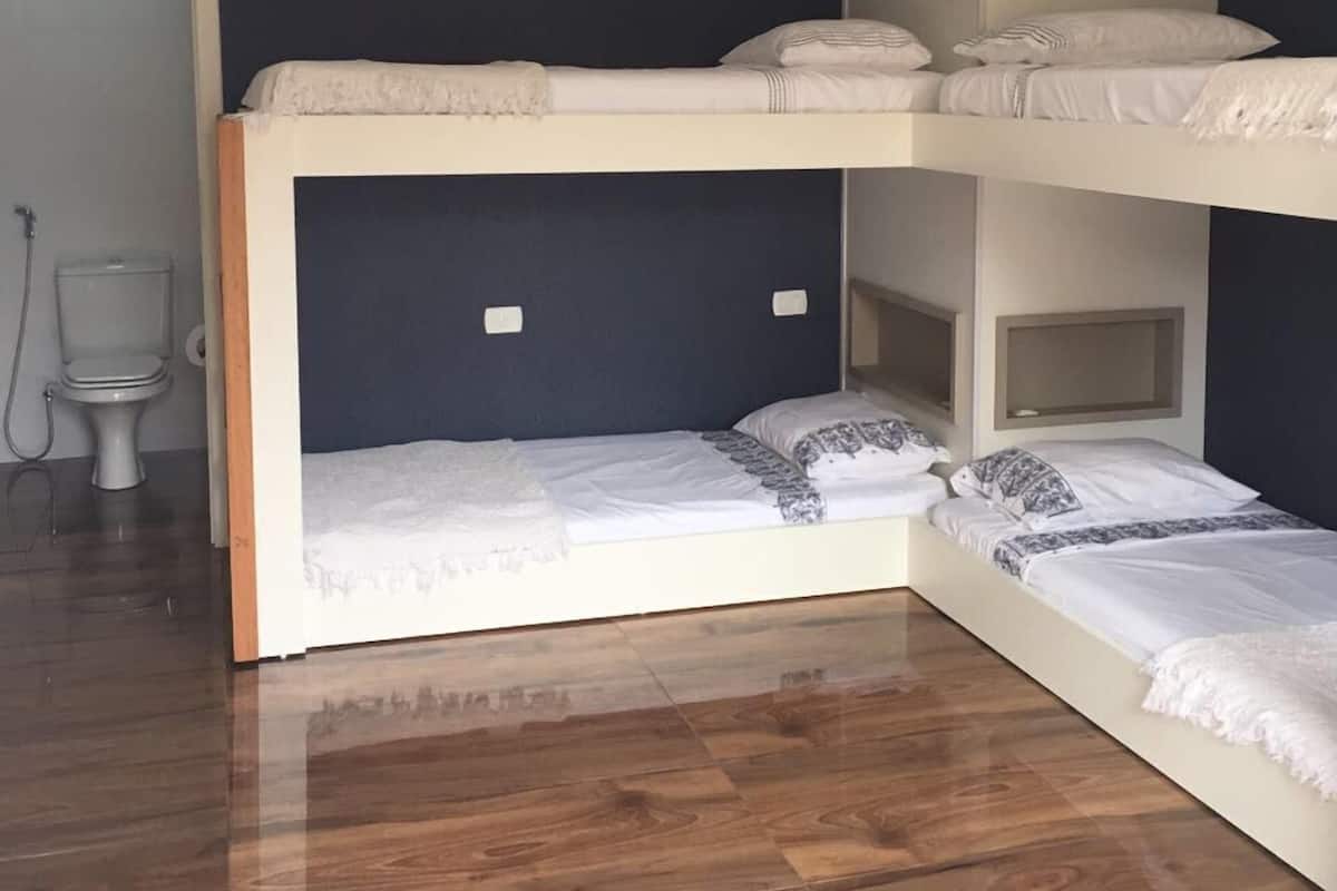 A bunk bed room with a wooden floor, a toilet, and a door.