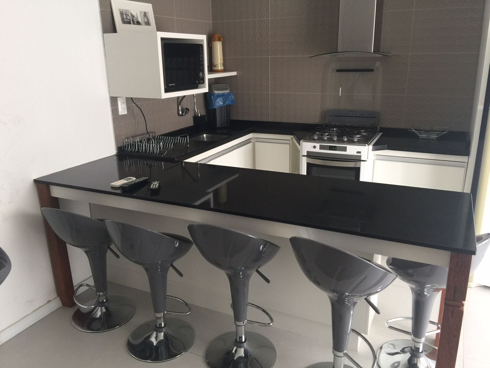 A kitchen with a black countertop, a stove, a microwave, and three bar stools.