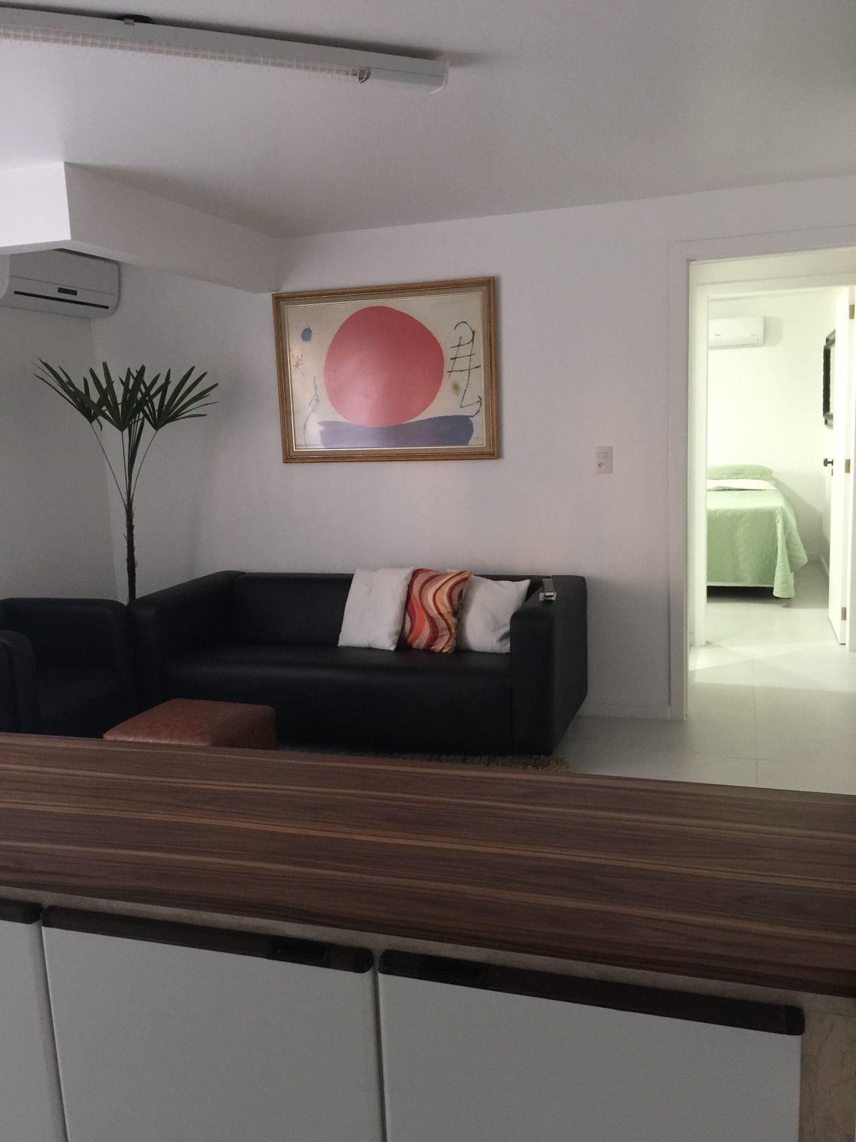 Ein Wohnzimmer mit einer schwarzen Couch, einem Holztisch, einer Zimmerpflanze und einem Bild an der Wand.