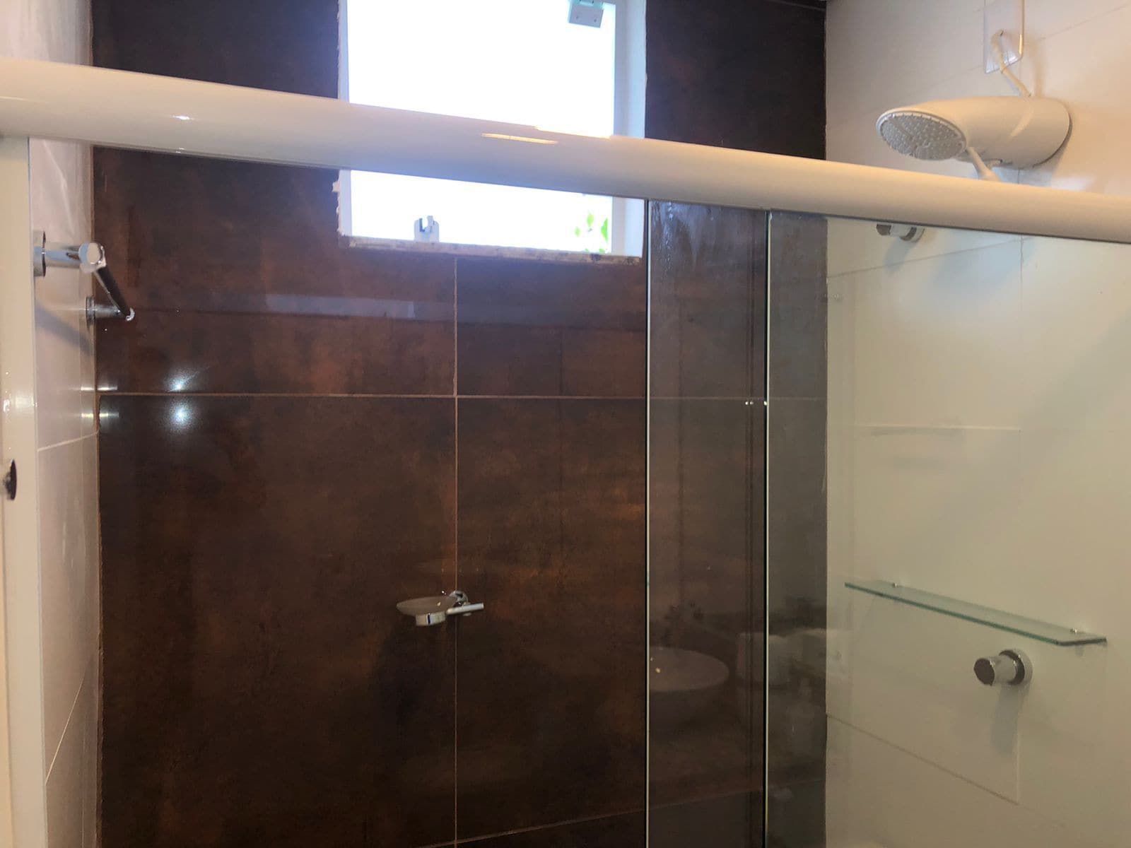 A modern bathroom with a glass shower enclosure, a glass shelf, and a handheld showerhead.