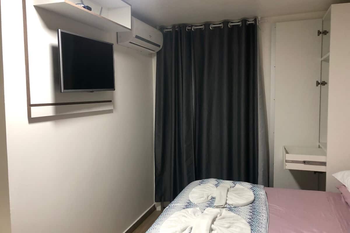 A hotel room with a bed, a TV mounted on the wall, a wardrobe, and a curtain.