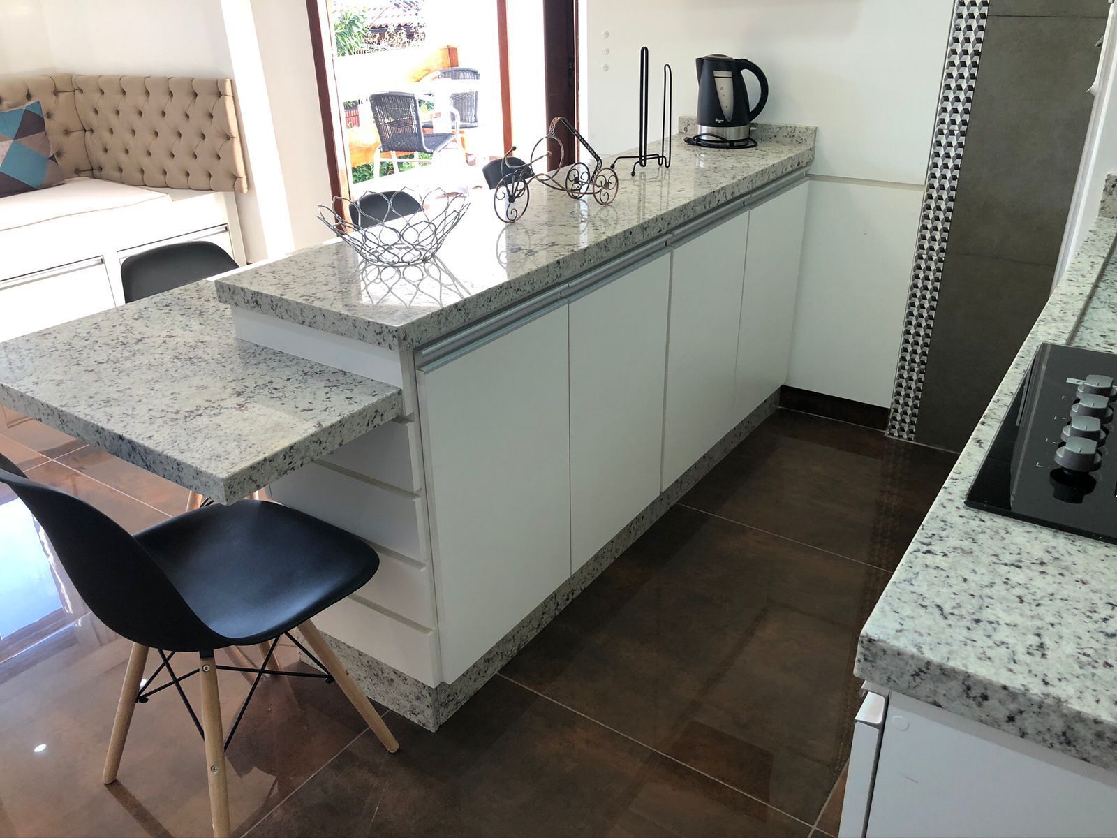 Una cocina con encimera de granito, armarios blancos, cafetera y hervidor.