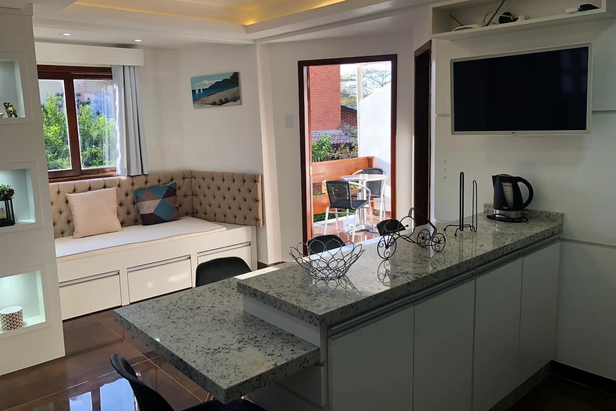 A modern kitchen with a central island, a dining area with a sofa, and a TV mounted on the wall.