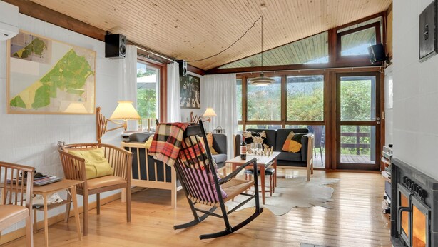 A cozy living room with wooden flooring, a fireplace, a rocking chair, and a dining area with a table and chairs. - Pet friendly home in Tisvildeleje (Tisvildeleje)