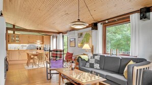 A cozy living room with a wooden ceiling, a grey sofa, a chess table, and a view of greenery outside. - Pet friendly home in Tisvildeleje (Tisvildeleje)