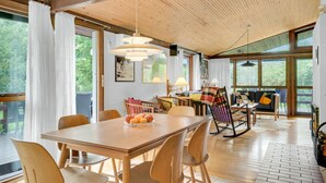 A spacious dining area with a wooden table and chairs, a rocking chair, and a view of the outdoors through large windows. - Pet friendly home in Tisvildeleje (Tisvildeleje)