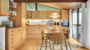 A modern kitchen with wooden cabinets, a dining table with chairs, and a large window. - Pet friendly home in Tisvildeleje (Tisvildeleje)