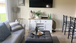 A living room with a sofa, ottoman, TV, and a dining area with chairs.