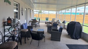 A covered patio area with wicker furniture, a metal table with decorative items, and a view of a wooden fence.