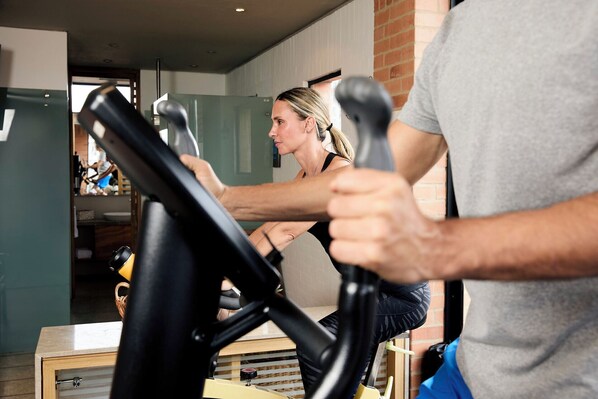 A person using an exercise bike in a room with a brick wall and a window. - Mercure bh Retiro (Bogotá)